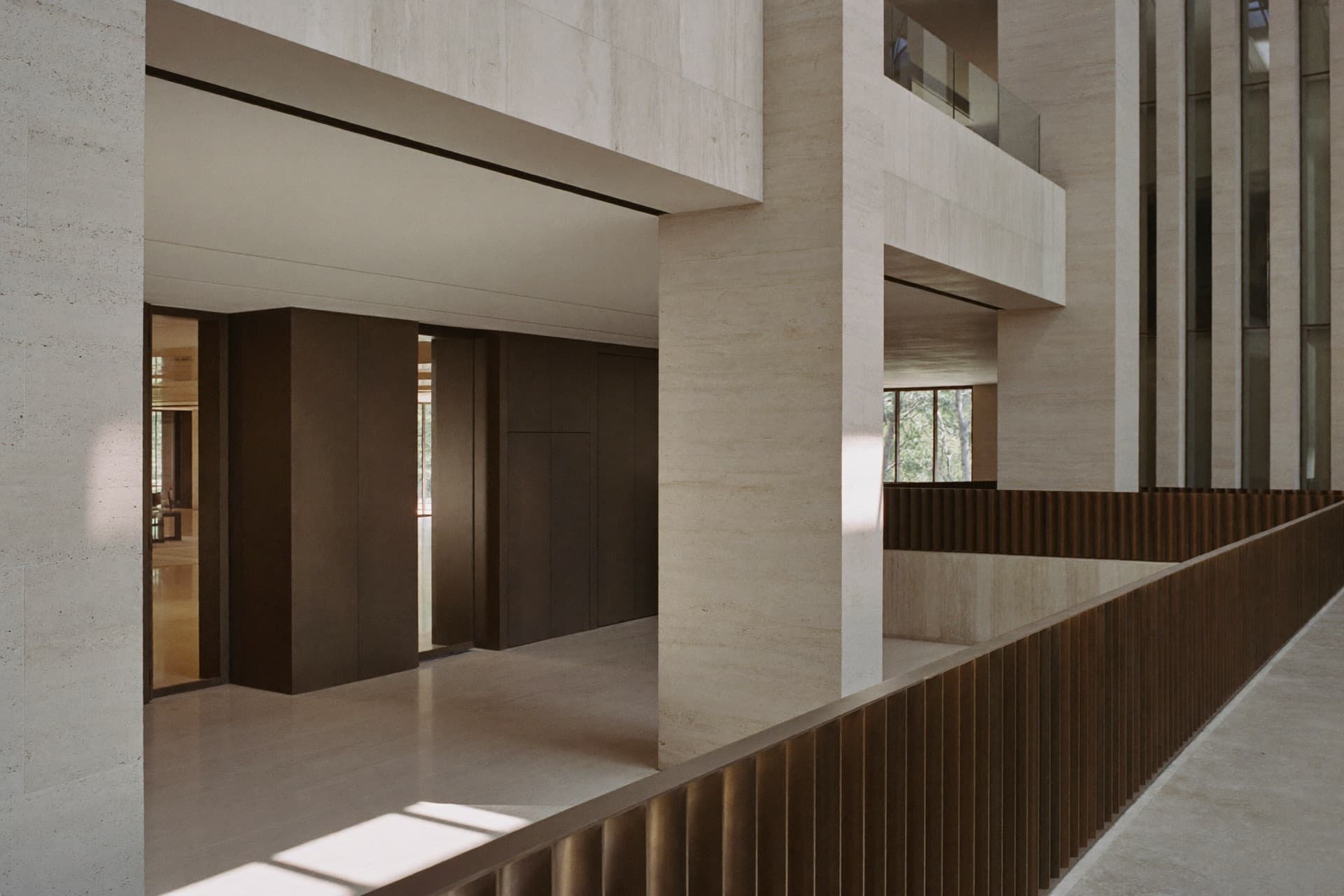 Travertine atrium of an institutional headquarters, bronze balustrade and morning light across the stone floor